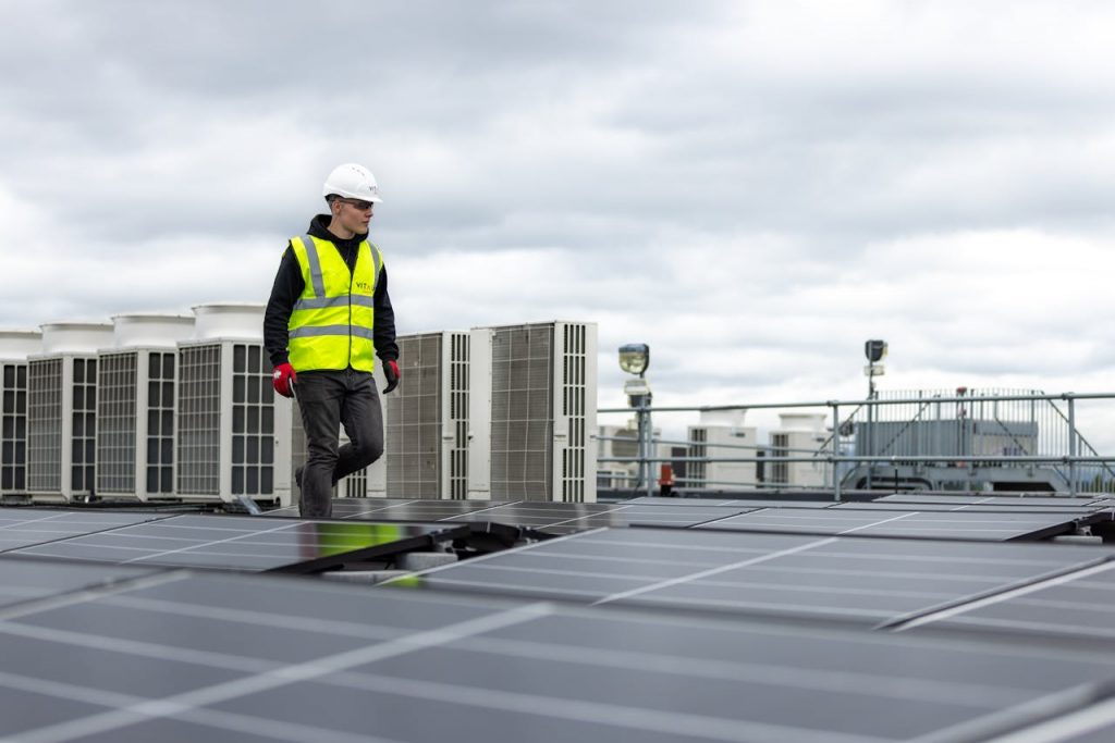 pexels-photo-19895917 Engineer in safety gear inspecting solar panels on a rooftop under a cloudy sky.