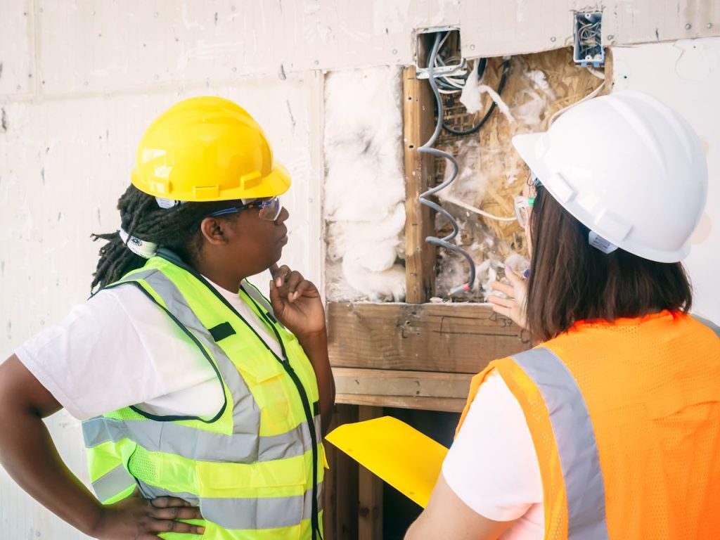 pexels-photo-8486934 Two female engineers wearing safety gear conduct a detailed inspection at a construction site.